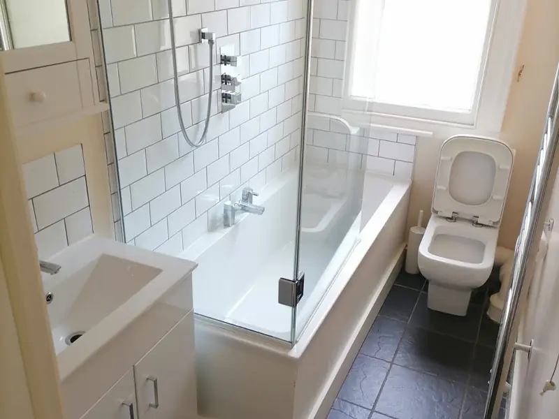 Bathroom with white metro tiles, a bath with glass shower screen, basin unit and toilet
