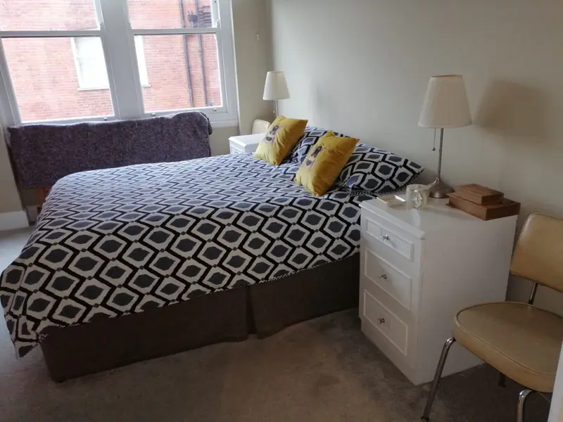 Bright bedroom with a made double bed, white bedside table and carpet