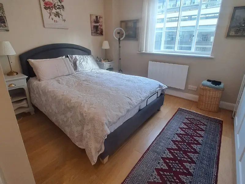 Bedroom with a made bed, wooden floor, runner rug and a large window