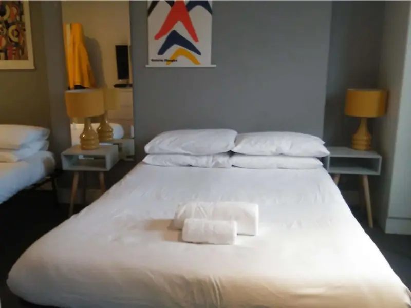 Double bed with white linen and rolled towels between yellow bedside lamps