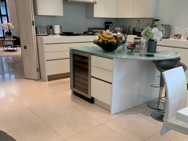 Clean kitchen with white units, a glass-topped island and a stone tiled floor