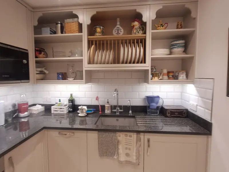 Kitchen with open shelves, a plate rack, dark granite worktop and white wall tiles