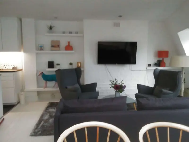 Open-plan living room with a sofa, two armchairs, shelves and a wall-mounted TV