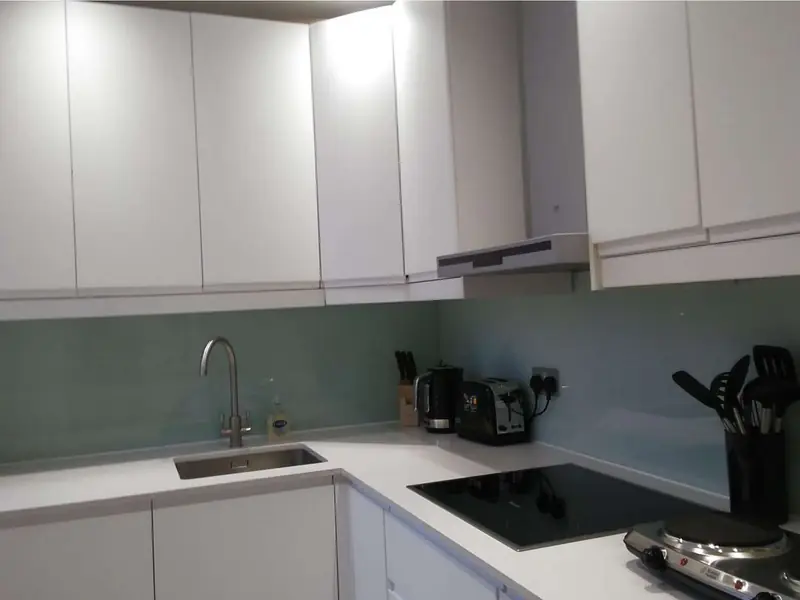White kitchen with clear worktops, sink, hob and glass splashback